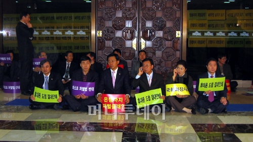 ↑원혜영 민주당 원내대표(사진 오른쪽에서 세번째)가 26일 오전 국회 본회의장 앞에서 연좌농성 도중 전화 통화를 하고 있다. 원 원내대표는 '휴대폰 도청 절대안돼'라는 문구가 적힌 포스터를 들고 있다.