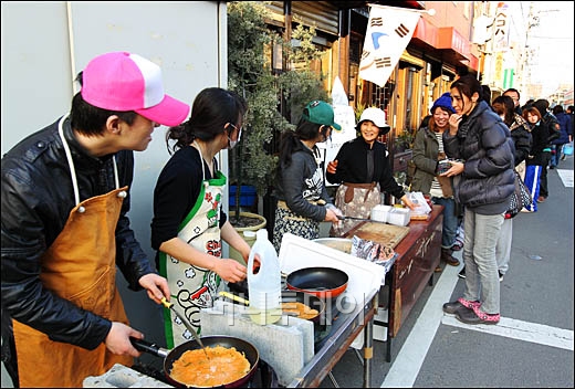 ↑태극기 달고... "아리가또 김치전"<br>
강진과 쓰나미가 휩쓸고 간 지 사흘째인 13일 일본 미야기현 센다이 북부 지역에서 한국인 부부가 운영하는 '부여' 식당 앞에 이재민 등이 길게 줄 서 있다. 태극기가 눈에 띄는 이 식당의 부부는 현지 생필품 공급이 원할하지 못하자 남은 김치로 전을 만들어 염가로 제공했다. ⓒ 센다이(일본)＝이동훈 기자 