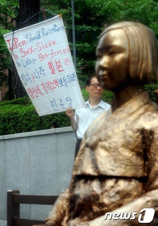 정대협(정신대문제대책협의회)이 위안부 할머니들의 소녀상에 말뚝을 설치해 논란을 일으킨 일본인 스즈키 노부유키에 대해 법적 대응에 나선 가운데 4일 오후 서울 종로구 중학동 일본 대사관 앞에서 정대협 주최로 열린 제 1029차 일본군 '위안부' 문제 해결을 위한 정기 수요시위에서 한 참가자가 위안부 소녀상 뒤에서 피켓을 들고 있다 . 2012.7.4/뉴스1  News1 손형주 인턴기자