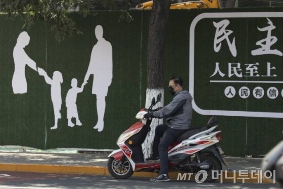 [베이징=AP/뉴시스]18일 중국 베이징 거리에서 마스크를 쓴 한 남성이 오토바이를 타고 '민주주의' '국민 우선'이라는 중국 정부 선전 문구가 적힌 벽화 앞에서 대기하고 있다. 중국 국가위생건강위원회는 베이징에서의 코로나19 학진 사례가 닷새 만에 20명대 초반으로 떨어졌다고 밝혔다. 2020.06.18.