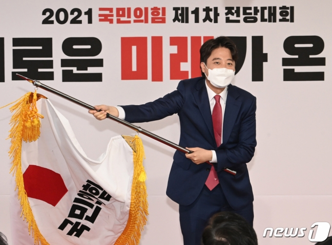 이준석 국민의힘 신임 대표가 11일 오전 서울 영등포구 국민의힘 당사에서 열린 전당대회에서 당기를 흔들고 있다. '30대·0선'의 이 대표는 역대급 전당대회 흥행을 주도한 끝에 헌정사상 최초의 30대 보수정당 대표에 올랐다. /사진=뉴스1