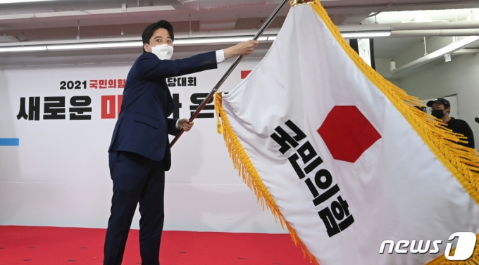 이준석 국민의힘 신임 대표가 11일 오전 서울 영등포구 국민의힘 당사에서 열린 전당대회에서 당기를 흔들고 있다. '30대·0선'의 이 대표는 역대급 전당대회 흥행을 주도한 끝에 헌정사상 최초의 30대 보수정당 대표에 올랐다./사진=뉴스1