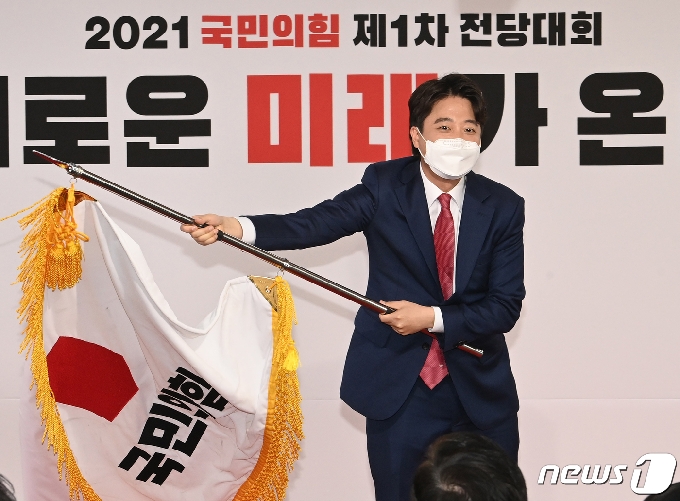 이준석 국민의힘 신임 대표가 11일 오전 서울 영등포구 국민의힘 당사에서 열린 전당대회에서 당기를 흔들고 있다. '30대·0선'의 이 대표는 역대급 전당대회 흥행을 주도한 끝에 헌정사상 최초의 30대 보수정당 대표에 올랐다. 2021.6.11/뉴스1 © News1 오대일 기자