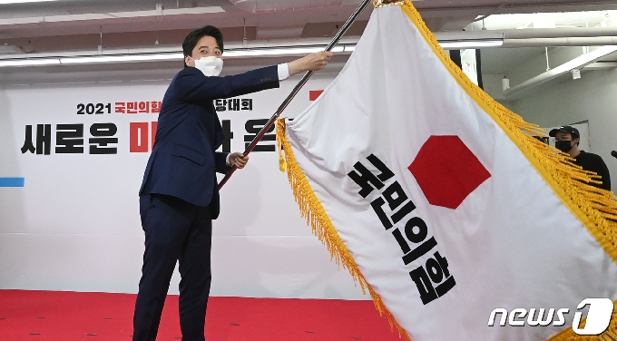 이준석 국민의힘 신임 대표가 11일 오전 서울 영등포구 국민의힘 당사에서 열린 전당대회에서 당기를 흔들고 있다. '30대·0선'의 이 대표는 역대급 전당대회 흥행을 주도한 끝에 헌정사상 최초의 30대 보수정당 대표에 올랐다. 2021.6.11/뉴스1 © News1 오대일 기자