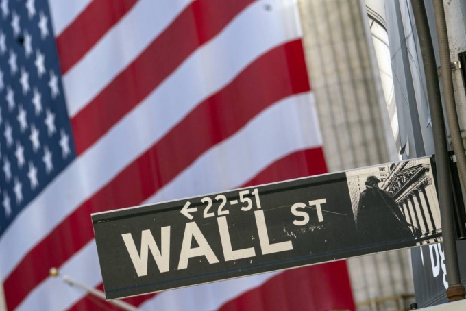 FILE - In this Monday, Sept. 21, 2020, file photo, a Wall Street street sign is framed by a giant American flag hanging on the New York Stock Exchange in New York. Stocks are falling in early trading on Wall Street Monday, Oct. 26, 2020, and deepening last weeks losses. (AP Photo/Mary Altaffer, File)