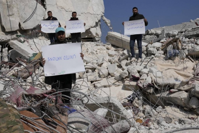 12일(현지시간) 시리아 아타렙에서 지진 피해 주민들이 유엔에 항의하는 손팻말을 들고 파괴된 집 잔해에 서서 시위하고 있다. /AP=뉴시스