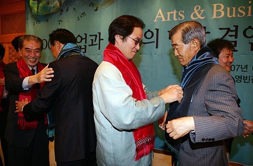 ↑이날 행사에 참여한 기업과 문화단체 대표들이 결연식의 의미로 붉은 머플러를
나누고 있다.