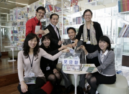 ↑웅진씽크빅 임직원들이 활짝 웃으며 모금함에 기부를 하고 있다.