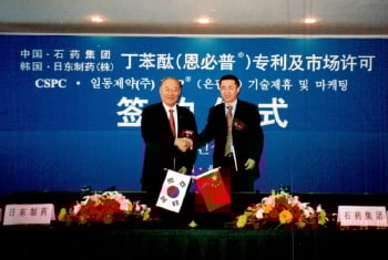 ↑이금기 일동제약 회장(왼쪽)과 위에진(岳進) 석약그룹 총재가 계약서에 서명 후 악수하고 있다.