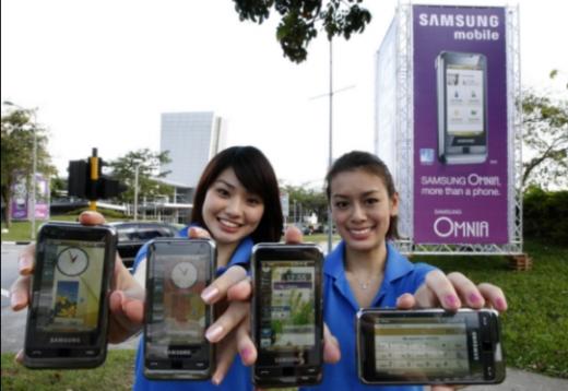 ▲싱가포르에서 열리는 동남아 최대 정보통신 전시회인 커뮤닉아시아 2008 개막을 하루 앞둔 16일 삼성전자 도우미들이 전시장 앞에서 삼성전자의 글로벌 전략폰인 '옴니아'를 선보이고 있다.