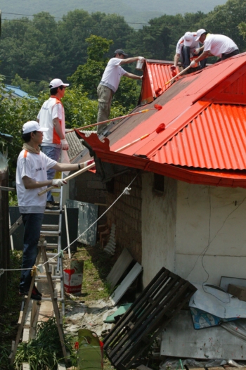 ▲KTF 임직원들이 23일 경기 김포 용강리 민통선 마을을 찾아 독거노인이 거주하는 주택의 지붕수리 및 도색작업을 하고 있다.