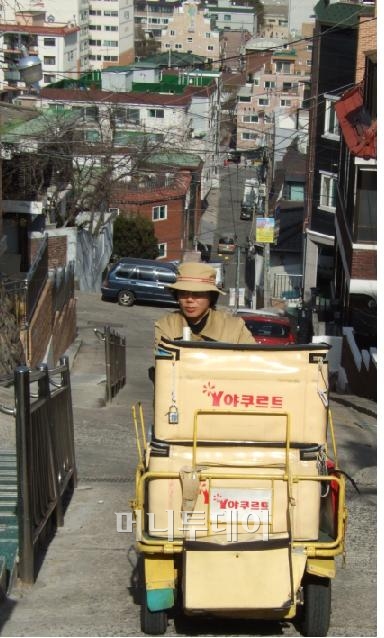 ▲'야쿠르트 아줌마' 윤성순씨가 화곡동 주택가에 야쿠르트를 배달하기 위해 급경사길을 오르고 있다. 윤씨는 20년간 이 길을 오르내렸다.