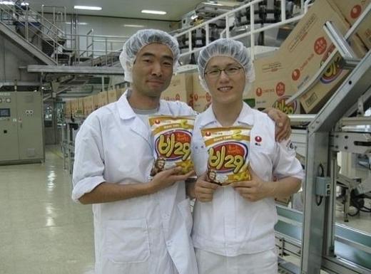 ▲'비29'의 연구·개발을 맡은 농심의 박준상 차장(왼쪽)이 공장에서 18년만에 다시 선보인 비29의 첫번째 생산품을 들고 웃고 있다. 박 차장은 이 사진을 '카레맛 과자 비29의 생산을 바라는 카페'에도 올렸다.