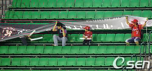 ↑ 프로야구 경기중 비가 내리자 현수막으로 비를 피하고 있는 관중들. 프로야구 관중 800만 시대에도 한국에는 여전히 돔구장이 하나도 없다. ⓒ사진제공=OSEN