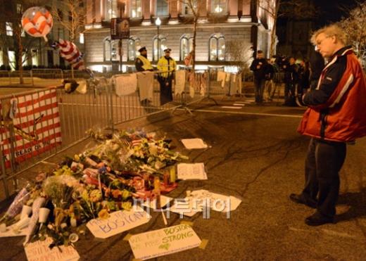 ↑16일 보스턴마라톤 테러현장을 봉쇄하는 바리케이드에 추모객들의 바친 조화와 애도문을 한 추모객이 바라보고 있다.