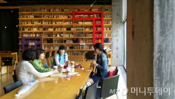 어린이도서연구회 회원들이 '지혜의 숲'을 방문해 동화책을 골라 놓고, 어린이 권장도서에 대해 이야기 나누고 있다. 서가 디자인은 훈민정음을 모티브로 했다. 뒤편에 'ㄱ'(기역) 모양이 보인다.