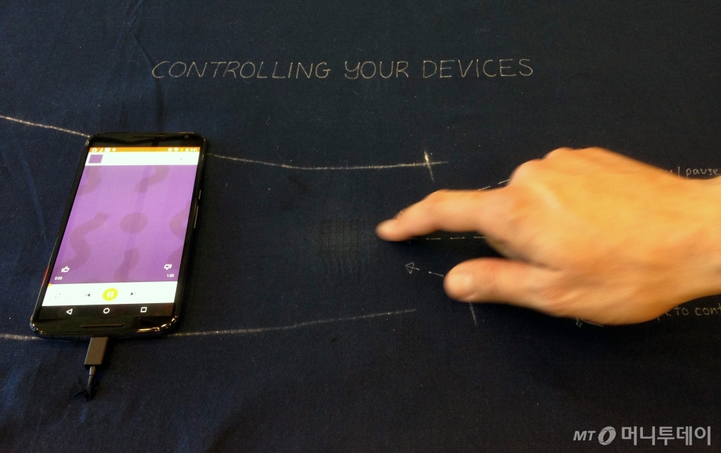 책상 위에 마우스를 사라지게 만들 구글의 새로운 기술 '프로젝트 잭쿼드'. 파란 천 위를 누르거나 옆으로 밀거나 아래위로 손가락을 쓸면, 스마트폰에 켜있는 음악이 다음 곡으로 넘어가기도 하고 켜지거나 꺼진다.