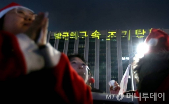 24일 저녁 서울 광화문광장에서 열린 9차 촛불집회에 산타 복장으로 참석한 시민들이 정부서울청사에 비친 문구 앞에서 구호를 외치고 있다./ 사진=홍봉진 기자