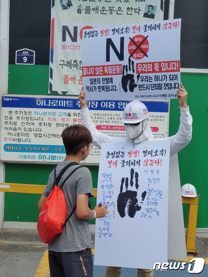 (광주=뉴스1) 허단비 기자 = 3일 오후 전남 구례에서 일본의 경제보복과 백색 국가 배제에 항의하며 이형용씨가 1인 시위를 하고 있다. 한 아이가 피켓에 서명을 하기 전 피켓문구를 읽고 있다.(독자제공)2019.8.4/뉴스1  <저작권자 © 뉴스1코리아, 무단전재 및 재배포 금지>