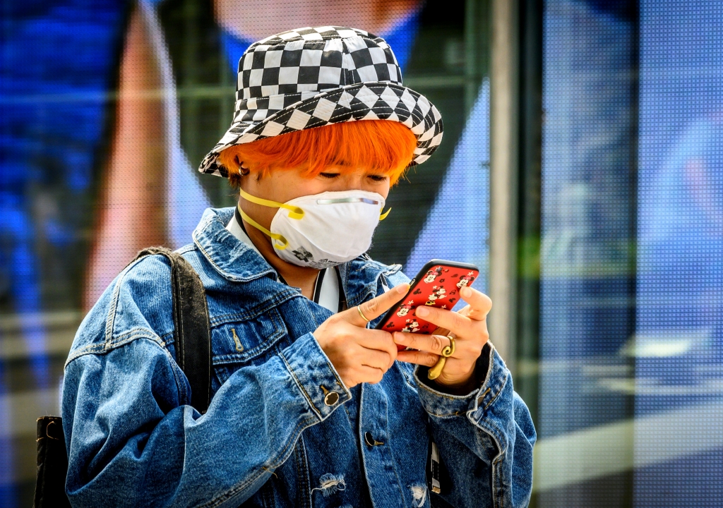 마스크를 쓴 한 여성이 자신의 휴대폰을 확인하고 있다. /사진=AFP