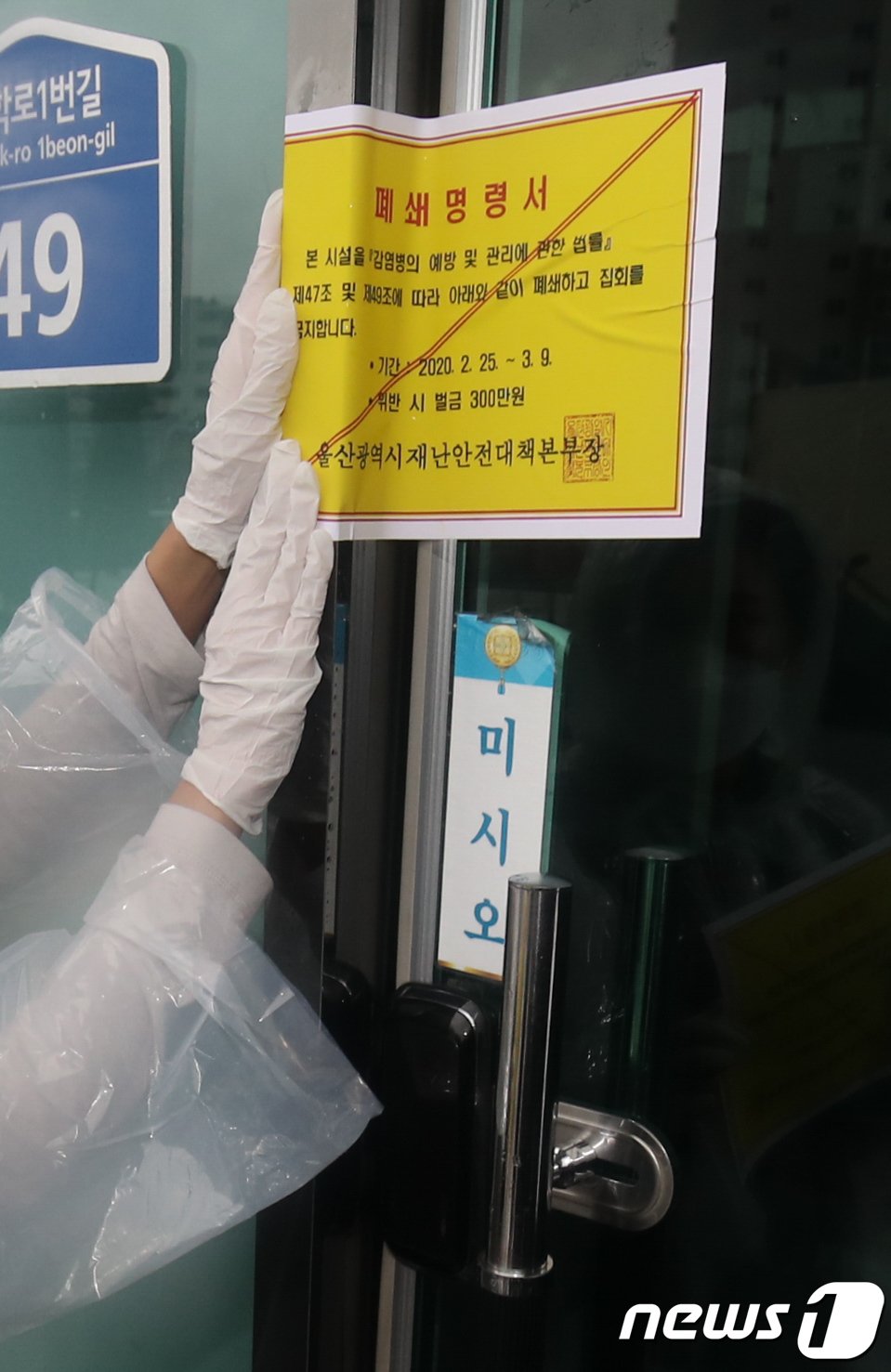 25일 신종 코로나바이러스 감염증(코로나19) 울산 확진자가 4명으로 늘어난 가운데 울산시청 공무원들이 남구 무거동 신천지 울산교회 출입문에 폐쇄명령서를 붙이고 있다. / 사진 = 뉴스 1