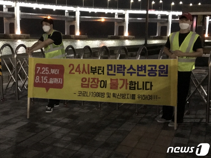 26일 새벽 부산 수영구 수변공원 입구에서 관할 기관 관계자들이 자정 이후 입구 제한 및 새벽2시까지 운영방침을 알리는 현수막을 들고 있다. 2020.7.26 © 뉴스1 이유진 기자