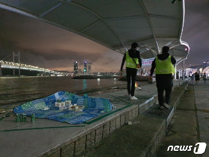 26일 새벽 2시가 지난 부산 수영구 수변공원 현장. 이날부터 수영구가 코로나19 확산 방지를 위해 수변공원 운영시간을 새벽 2시까지로 제한하면서, 현장에 있던 시민들이 쓰레기를 치우지 않은 채 급하게 자리를 떠난 곳을 안내요원들이 지나가고 있다. 2020.7.26 © 뉴스1 노경민 기자