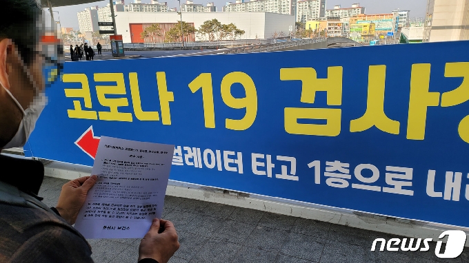 수원역에 마련된 화성시 임시 선별검사소 안내 현수막 앞에서 검체 검사를 마친 한 시민이 배부받은 검사 후 주의사항을 살펴보고 있다. © 뉴스1