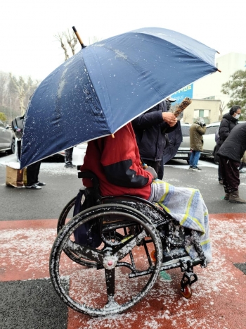 안나의 집에서 만든 도시락을 받기 위해 우산을 쓰고 휠체어를 탄 채 기다리는 노숙인./사진=김하종 신부 페이스북