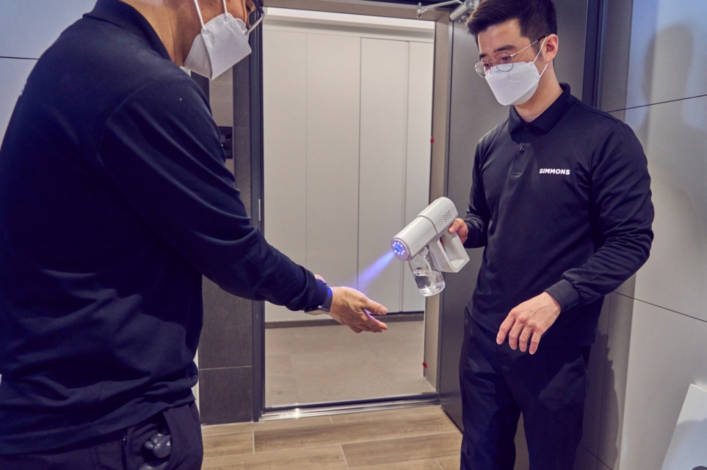 시몬스 배송 매니저들이 고객 집에 들어가기 전 장갑을 벗고 손소독하고 있다. 시몬스는 2020년 프리미엄 배송 서비스를 시작했다. 다른 침구 업체들처럼 시몬스도 그 전까지는 일부 상품은 가맹점주들이 배송을 했다. 배송 서비스를 통일할 수 없었다. 시몬스는 가맹점을 없애고 전부 직영 체제로 바꾸고 직배송을 시작했다. 배송 서비스의 하나로 '청결 방역'을 했는데 코로나19 기간 큰 호응을 얻었다./사진제공=시몬스.