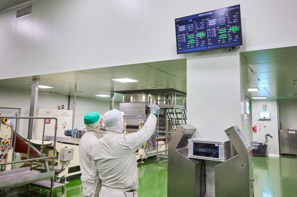 삼양식품 직원들이 제면증숙 공정 설비 앞에서 제조 현황을 살펴보고 있다. 상단에 부착된 화면에 공정 가동률 등이 실시간으로 표시된다. /사진제공=삼양식품