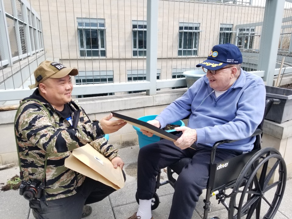 휠체어에 탄 참전용사에게 사진 액자를 전하는 라미 현 작가. 그는 이 순간에 변하는, 참전용사들의 자긍심 가득한 눈빛이 좋다고 했다./사진=라미 현 작가