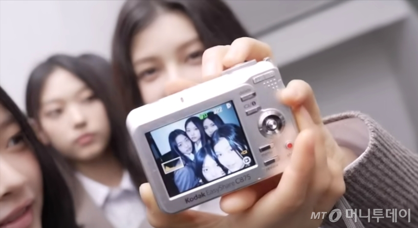 아이돌그룹 뉴진스의 '디토' 뮤직비디오에서는 5명의 멤버들이 빈티지 디카나 캠코더를 활용해 촬영을 하고 오래된 티비를 통해 촬영한 영상을 상영하는 장면이 등장한다. 뮤직비디오 비하인드 영상에서 뉴진스 멤버들이 빈티지 디카로 사진을 찍고 있다./사진=뉴진스 유튜브 영상 갈무리