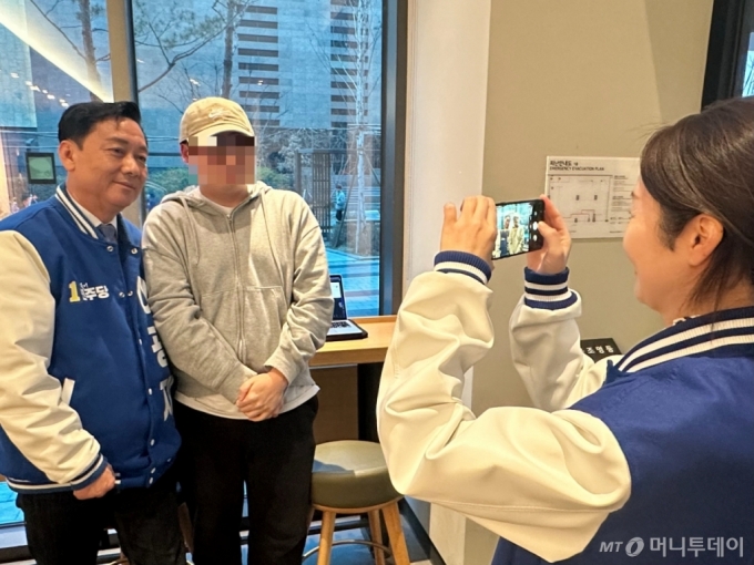 더불어민주당 경기 성남분당갑 이광재 후보가 판교역 인근 한 카페에서 한 시민과 사진을 찍는 모습. 민주당 강선우 의원이 시민의 휴대폰으로 사진을 찍고 있다. /사진=김도현 기자