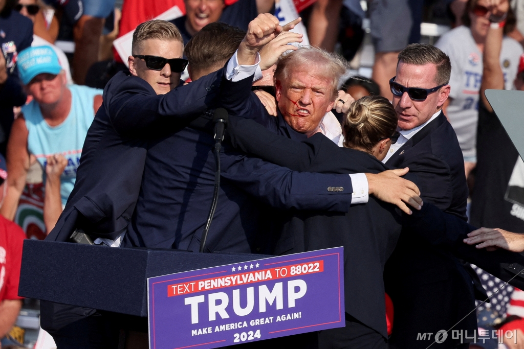(버틀러 로이터=뉴스1) 장시온 기자 = 13일(현지시간) 미국 공화당 대선 후보인 도널드 트럼프 전 대통령이 펜실베이니아주 버틀러에서 선거 유세 도중 오른쪽 귀에 총을 맞은 뒤 경호원에 둘러 쌓인 채 주먹을 쥐고 있다. 이날 총격으로 현장에 있던 지지자 1명이 숨지고 2명이 중상을 입었다. 2024.07.15. ⓒ 로이터=뉴스1 Copyright © 뉴스1. All rights reserved. 무단 전재 및 재배포, AI학습 이용 금지. /사진=(버틀러 로이터=뉴스1) 장시온 기자