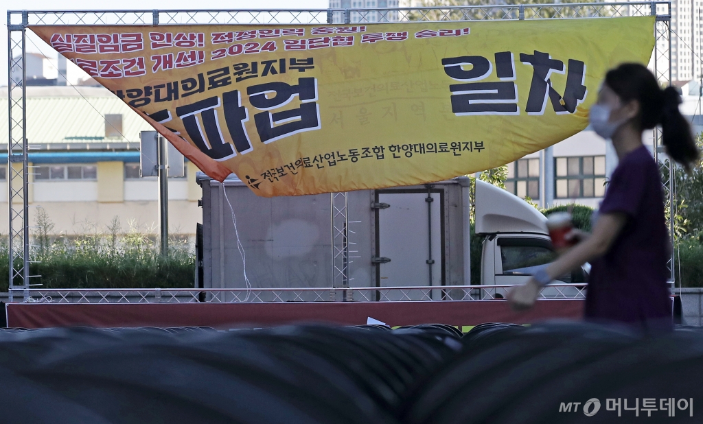 (서울=뉴스1) 오대일 기자 = 보건의료노조가 총파업을 사실상 철회한 29일 오전 서울 성동구 한양대병원에서 한 간호사가 파업 독려 현수막이 걸린 노조의 총파업 행사장 사이를 걸어가고 있다.   보건의료노조에 따르면 전날부터 밤새 이어진 노동위원회 조정 결과 쟁의조정을 신청한 62개 병원 사업장 가운데 59곳이 임금 및 단체협약 체결에 성공했다. 2024.8.29/뉴스1  Copyright © 뉴스1. All rights reserved. 무단 전재 및 재배포,  AI학습 이용 금지. /사진=(서울=뉴스1) 오대일 기자