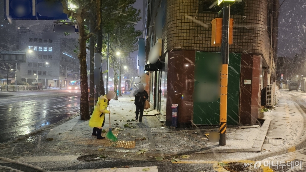 27일 오전 6시30분 용산구 원효동의 거리. 눈보라가 거세게 내리자 교통경찰이 눈을 쓸고 있다. 그 옆으로 중년 남성이 우산을 비스듬히 쓴 채 지나가고 있다./ 사진=송정현 기자