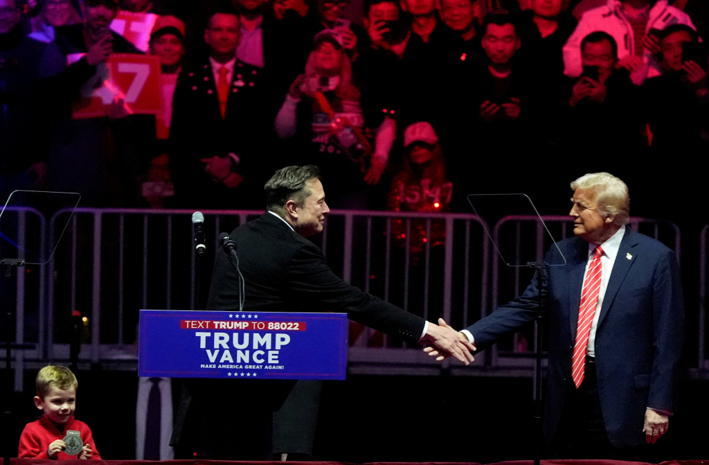 도널드 트럼프 미국 대통령 당선인이 19일(현지시간) 워싱턴 '캐피털 원 아레나' 경기장에서 열린 MAGA 대선 승리 축하 집회서 연설을 하는 일론 머스크 테슬라 CEO와 악수를 하고 있다. /로이터=뉴스1