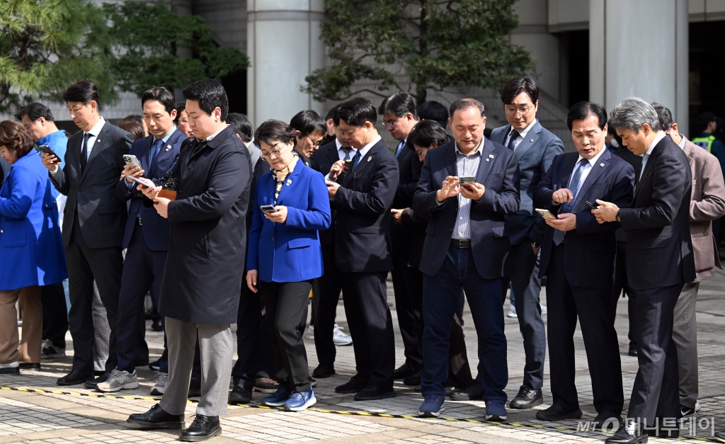 [서울=뉴시스] 사진공동취재단 = 이재명 더불어민주당 대표의 공직선거법 위반 혐의 항소심 선고 공판이 열린 26일 서울 서초구 서울고등법원 앞에서 더불어민주당 의원들이 휴대폰으로 재판 관련 뉴스를 보고 있다. 2025.03.26. photo@newsis.com /사진=최동준