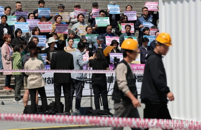 세계 산재 노동자의 날인 28일 서울 종로구 세종문화회관 앞에서 열린 '산재 노동자의날 국가기념일 제정 원년, 산재 피해자·유가족 기자회견' 인파 앞으로 광화문 광장에서 작업 중인 노동자들이 안전모를 쓰고 이동하고 있다. 산재 노동자의 날은 전 세계에서 작업 중 죽거나 다친 노동자들을 추모하는 날로, 우리나라에서는 올해 처음으로 국가기념일로 지정됐다. 2025.4.28/사진=뉴스1 Copyright © 뉴스1. All rights reserved. 무단 전재 및 재배포, AI학습 이용 금지.