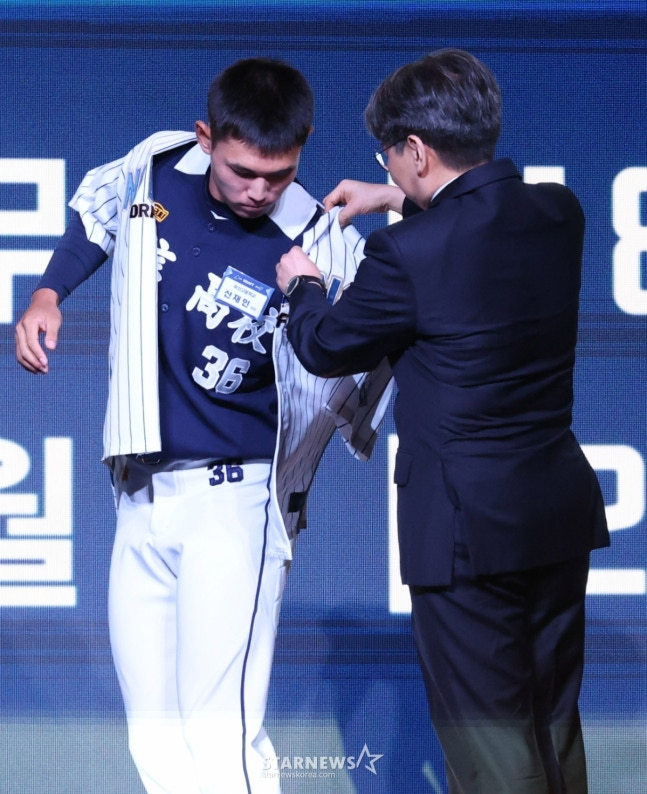 '2026 KBO 신인 드래프트'가 17일 서울 송파구 롯데호텔 월드 크리스탈볼룸에서 열렸다. 신재인(유신고)이 전체 2순위로 NC에 지명된 후 NC 임선민 단장의 도움을 받아 유니폼을 입고 있다. /사진=김진경 대기자