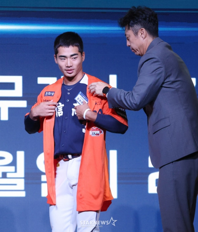 '2026 KBO 신인 드래프트'가 17일 서울 송파구 롯데호텔 월드 크리스탈볼룸에서 열렸다. 오재원(유신고)이 전체 3순위로 한화에 지명된 후 손혁 단장의 도움으로 유니 폼을 입고 있다.