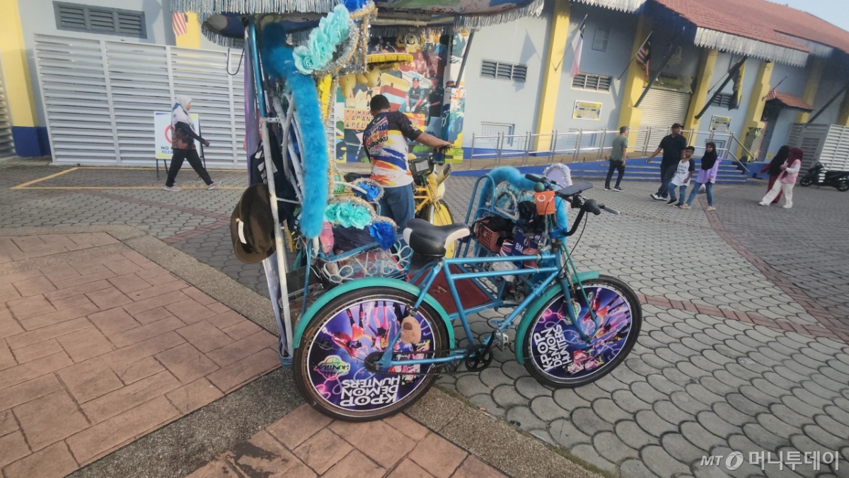 말레이시아 남서부에 위치한 작은 항구 도시인 말라카.  현지 말레이시아 기사가 관광객을 태우고 운전하는 인력거(tricycle) 바퀴에 케이팝 데몬 헌터스(케데헌) 포스터가 둘러져있다. 인력거 스피커에서 케데헌 OST인 '골든'이 흘러나오고 있다./사진=송정현 기자