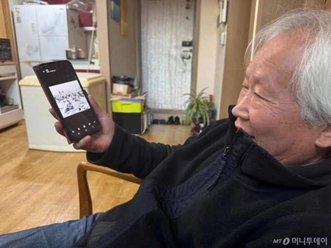 문혁씨(73)가 지난해 12월 윤석열 전 대통령 탄핵 촉구 집회 사진을 보고 있다. 휴대전화 속 사진은 은박지를 덮은 채 눈을 맞고 있는 집회 참여 청년들의 모습. /사진=최문혁 기자.