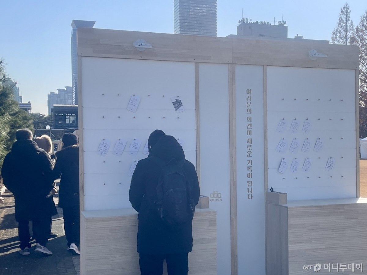 3일 서울 영등포구 국회 중앙잔디광장에서 시민들이 비상계엄 해제 1주년을 맞아 사진전을 감상하고 기록을 남기는 모습./사진=이현수 기자.