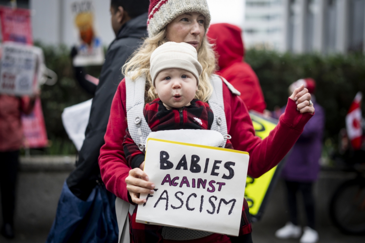 2025년 3월4일(현지 시간) 캐나다 브리티시컬럼비아주 밴쿠버에 있는 미국 대사관 앞에서 아이를 안은 여성이 손팻말을 들고 반미(反美) 시위를 하면서 춤추고 있다. 캐/AP=뉴시스 