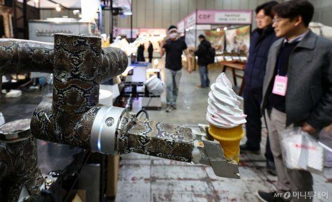 (고양=뉴스1) 김도우 기자 = 22일 경기 고양시 킨텍스에서 열린 2026 카페디저트페어에서 관람객들이 로봇이 전달하는 아이스크림을 지켜보고 있다. 2026.1.22/뉴스1  Copyright (C) 뉴스1. All rights reserved. 무단 전재 및 재배포,  AI학습 이용 금지. /사진=(고양=뉴스1) 김도우 기자