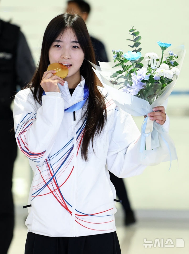 최가온이 입국장을 빠져나온 뒤 금메달을 깨물어보며 포즈를 취하고 있다. /사진=뉴시스