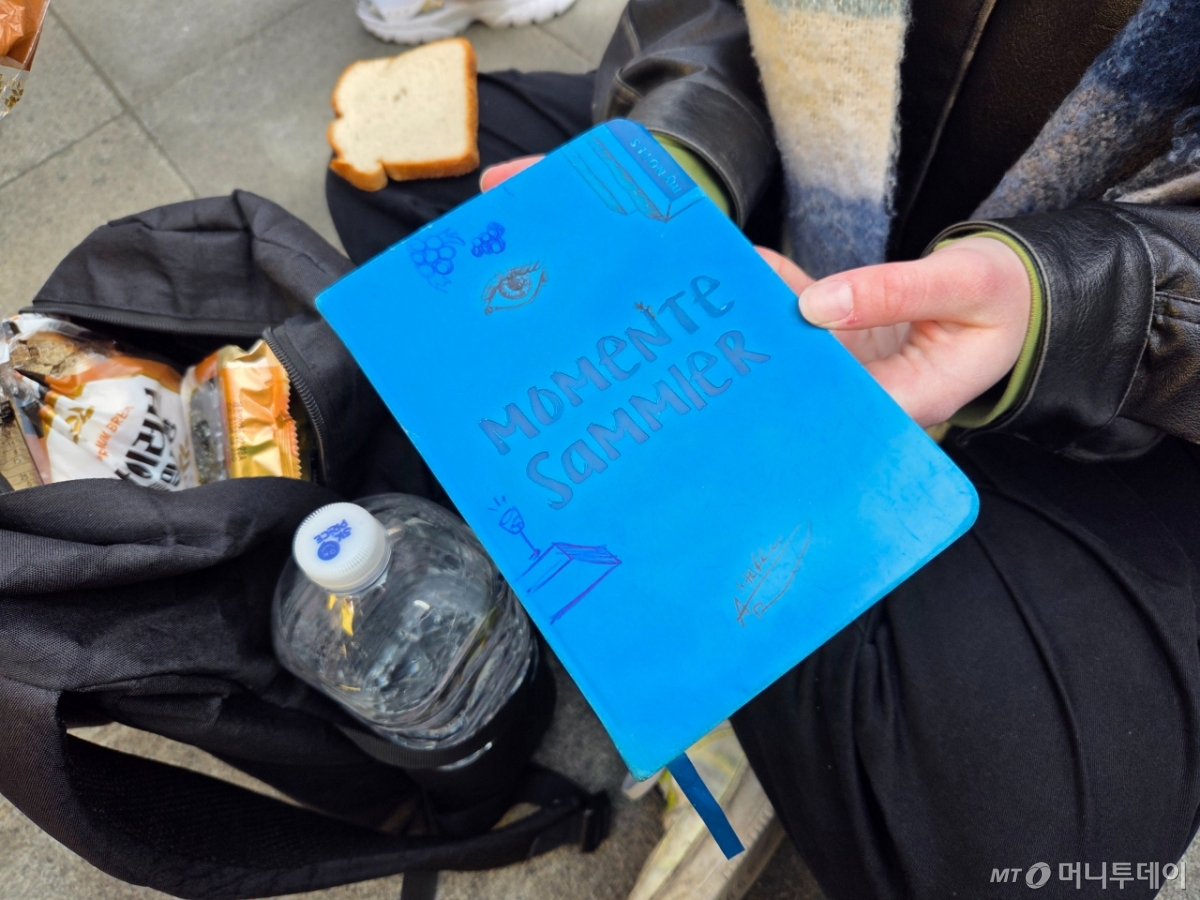 아밀리씨는 펜스 앞에 주저 앉아 식빵을 먹고 있었다. 그림 그리기를 좋아하는 아밀리씨는 오늘 BTS의 공연을 노트에 그려 추억으로 남길 생각이다./사진=김서현 기자.
