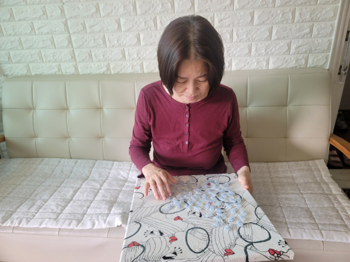  정은교 작가(62)가 자신의 작품 '눈물 수'를 들고 있는 모습. 인공눈물 용기로 만들어진 해당 작품에 대해 정 작가는 "눈물로 수를 놓는 이미지를 연상했다"며 "어둠 속을 헤매면서도 스스로 해내고 있다는, 감동의 의미로서의 눈물을 떠올렸다"고 설명했다./사진제공=정은교 작가.